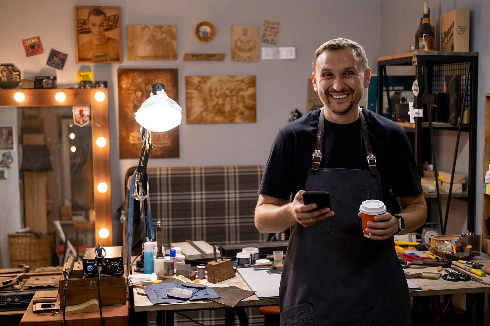 Emprendedor sonriendo con su celular y un café en su taller